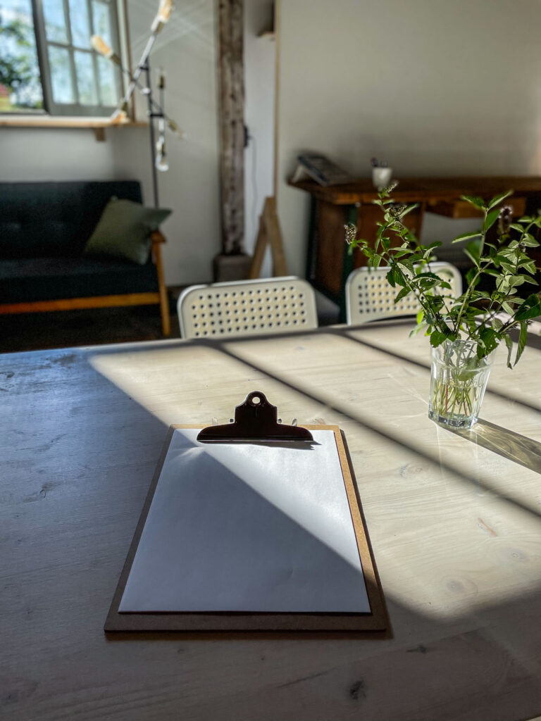 Heller Arbeitsbereich mit Clipboard, Tageslicht und Pflanzen bei Bahnhofszeit – inspiriert zum kreativen Arbeiten in ruhiger Atmosphäre.