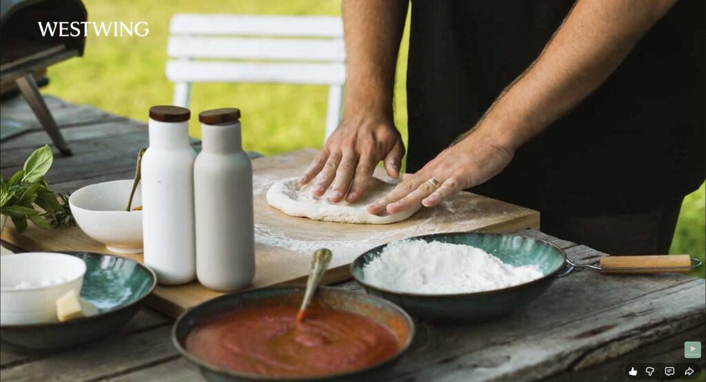 Hände formen frischen Pizzateig auf bemehltem Holzbrett im Garten während eines Westwing Outdoor-Cooking-Shootings.