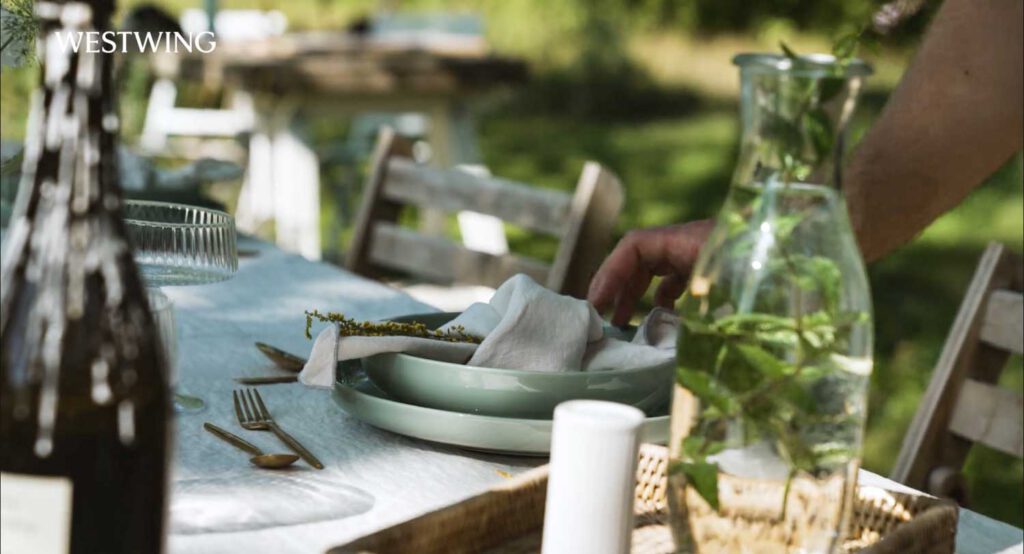 Westwing Shooting Location. Detailaufnahme eines eleganten gedeckten Gartentisches mit grünen Tellern, Leinenservietten und goldenen Besteck im Westwing Video.